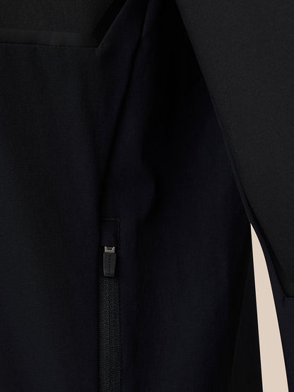 Close-up detail of a black garment with a vertical zipper and a small fabric pull tab, shown against a dark background.