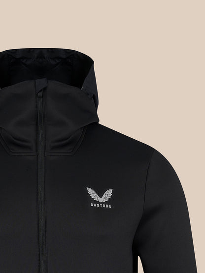 Close-up of a black hooded jacket with a front zipper and a small white winged logo reading CASTORE on the left chest, shown against a plain beige background.