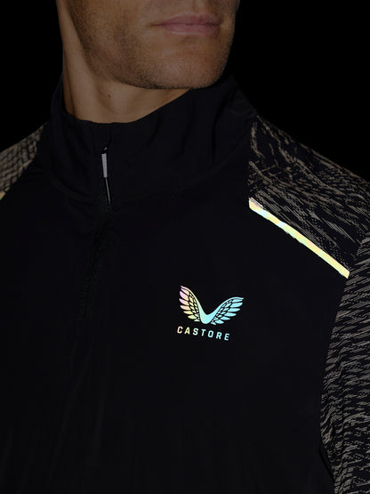 Close-up of a man wearing a black Castore athletic jacket with reflective gold/yellow shoulder stripes and a colorful wing logo on the chest.