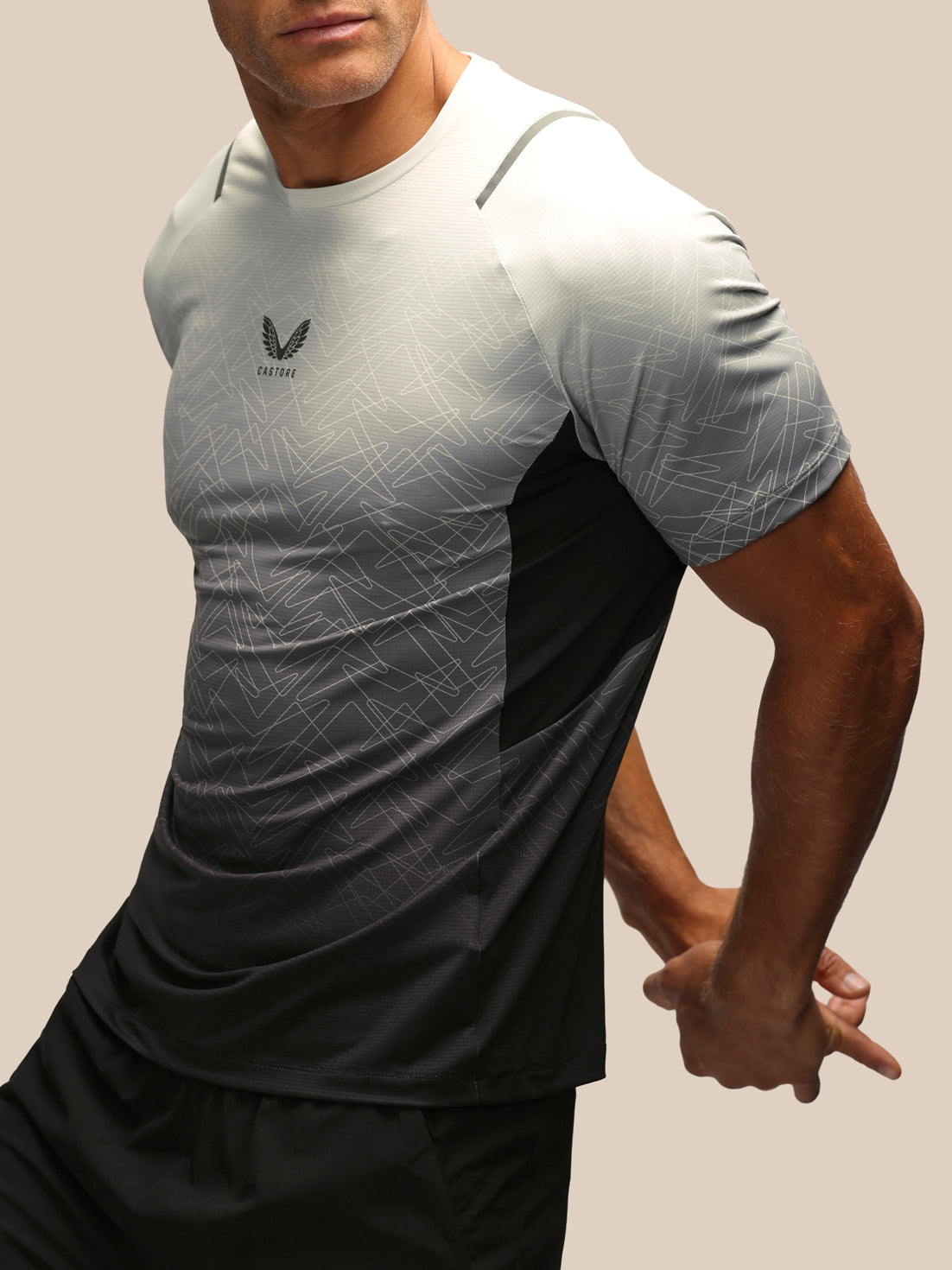 A close-up of a man wearing a short-sleeve athletic t-shirt with a gray and black gradient design, featuring a subtle geometric pattern and a black wing logo on the chest.