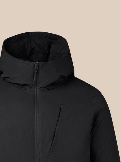 Close-up of a black hooded jacket with a front zipper and a vertical zip chest pocket, shown against a solid beige background.