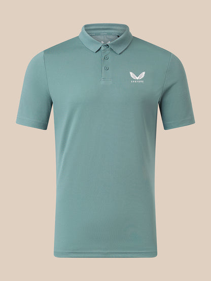 A short-sleeve polo shirt in a muted teal-green color, featuring a white wing logo and the brand name 'CASTORE' on the left chest, displayed on a solid beige background.
