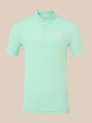 A mint green short-sleeve polo shirt with a small white embroidered logo on the left chest, displayed on a solid beige background.