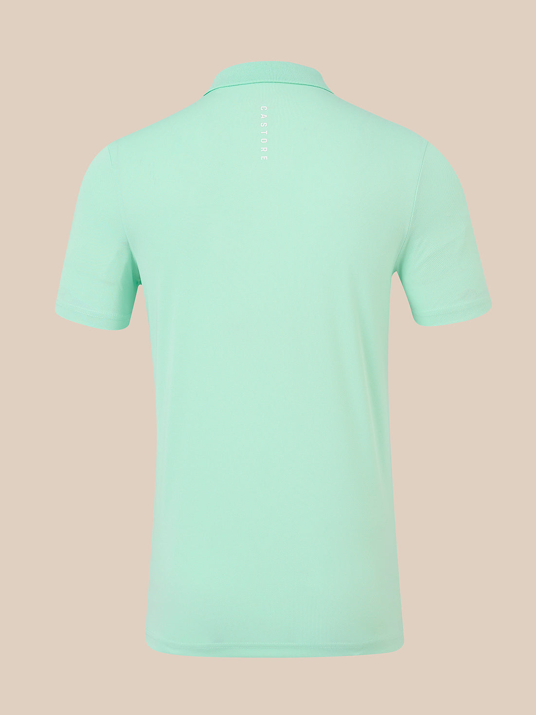 A mint green short-sleeve polo shirt shown from the back, featuring a vertical white 'CASTORE' logo printed on the upper back, set against a solid pale peach background.