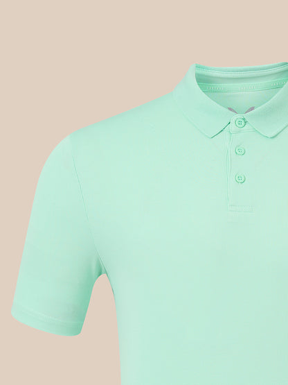 A close-up of a mint green short-sleeve polo shirt on a solid pale peach-beige background.