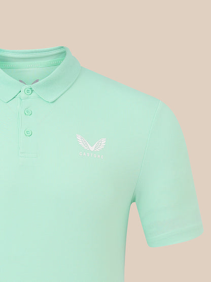 A mint green short-sleeve polo shirt with a white embroidered winged logo and the word 'CASTORE' on the left chest, shown against a solid pale peach background.