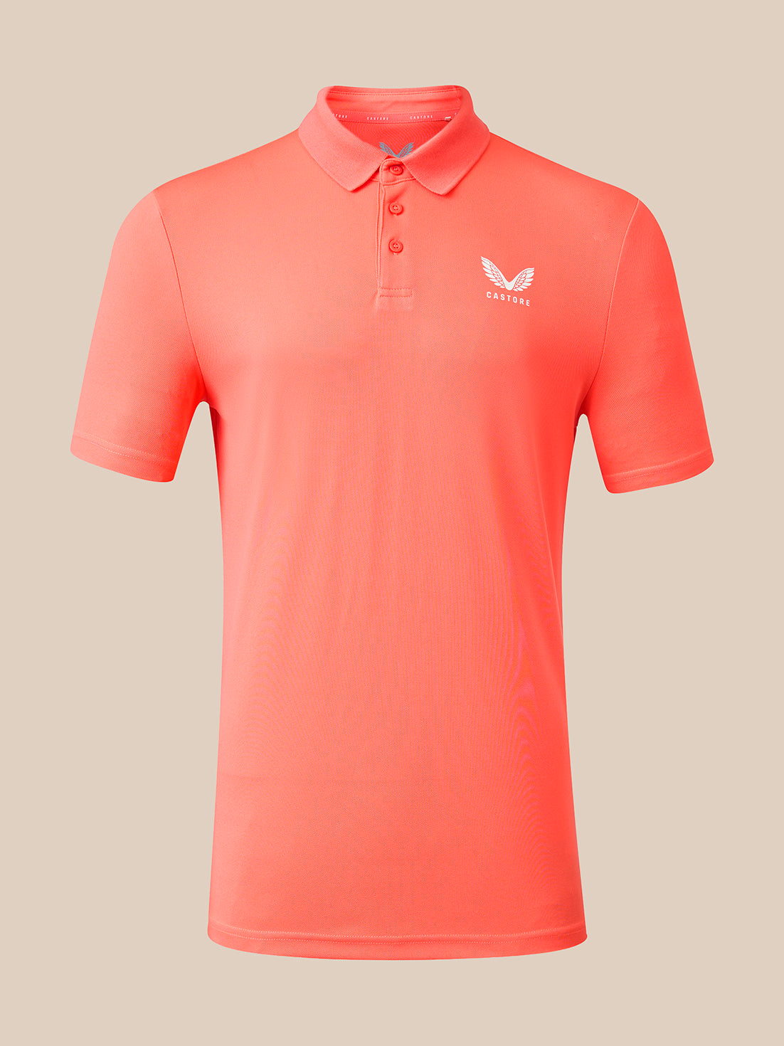 A coral pink short-sleeve polo shirt with a three-button placket and a small white wing logo on the left chest, displayed on a neutral beige background.