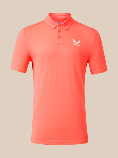 A coral pink short-sleeve polo shirt with a three-button placket and a small white wing logo on the left chest, displayed on a neutral beige background.