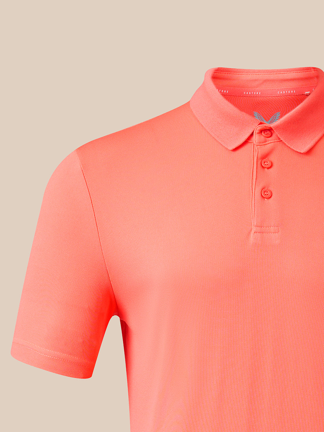 A close-up of a coral pink short-sleeve polo shirt on a neutral beige background.