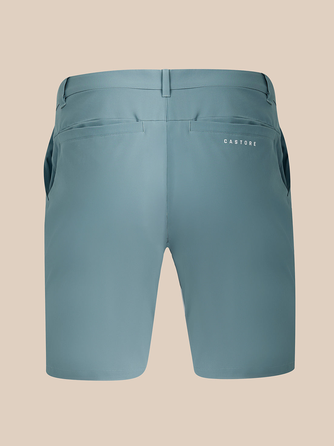Back view of a pair of Castore blue-gray athletic shorts on a solid beige background.