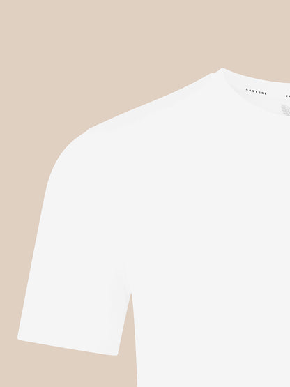 A close-up of a white short-sleeve crewneck t-shirt on a solid beige background.