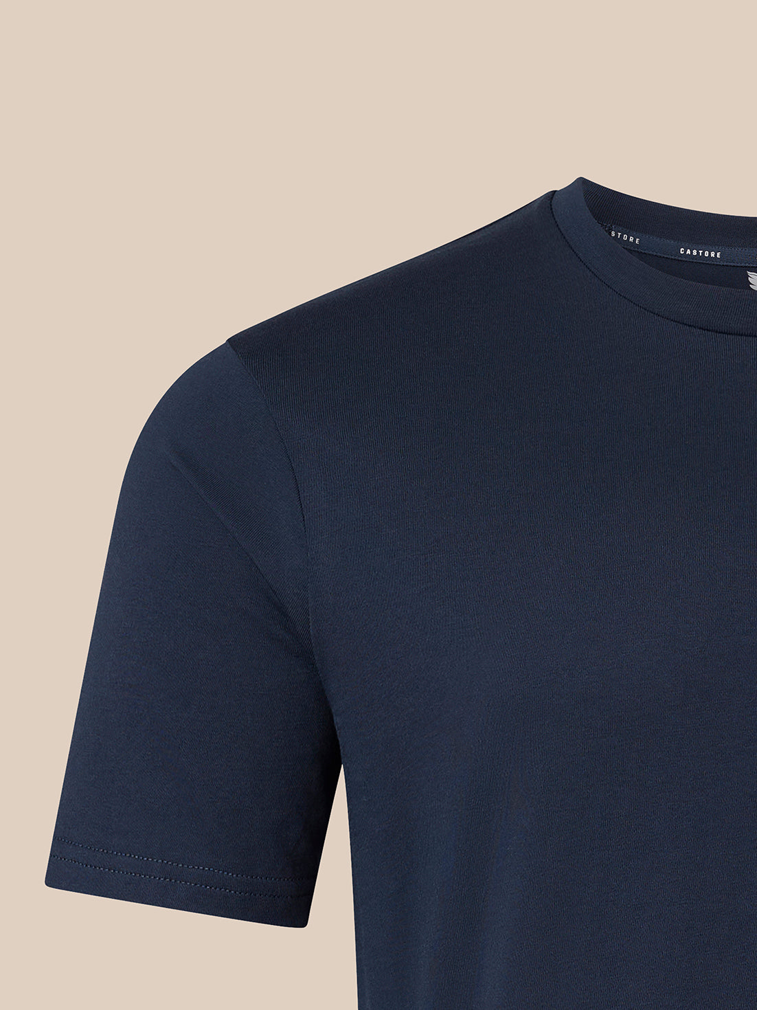 Close-up of a black short-sleeve crewneck t-shirt on a light beige background, showing the inner collar label with the brand name CASTORE.