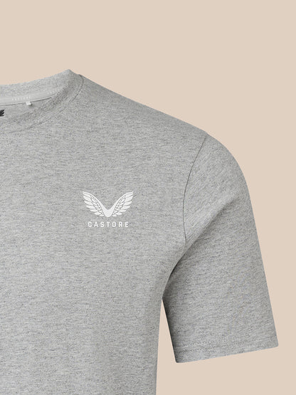 A close-up of a heather gray crewneck t-shirt featuring a white winged logo and the word 'CASTORE' printed on the left chest, set against a solid beige background.