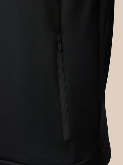Close-up of a black zippered pocket on a black garment, with a small portion of a light beige background visible on the right side.