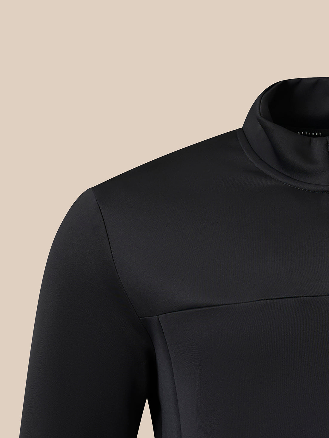 Close-up of a black long-sleeve top with a mock neck collar, shown on a mannequin or model against a solid beige background.