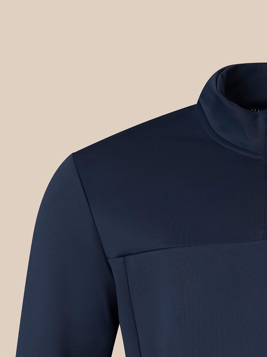 Close-up of a navy blue long-sleeve top with a mock neck collar and a horizontal seam across the chest, shown against a solid beige background.