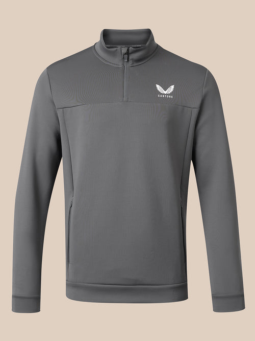 A dark gray long-sleeve quarter-zip pullover sweatshirt with a white winged logo on the left chest reading 'CASTORE', displayed against a solid beige background.