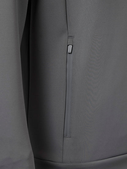 Close-up of a gray jacket or outerwear garment showing a vertical zip pocket with a small rectangular brand tab.