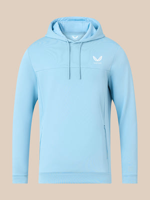A light blue athletic pullover hoodie with a white winged logo on the left chest, displayed on a solid beige background.