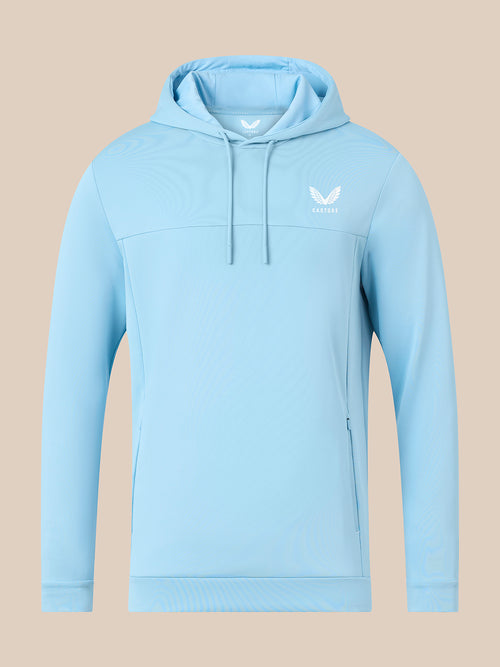 A light blue athletic pullover hoodie with a white winged logo on the left chest, displayed on a solid beige background.