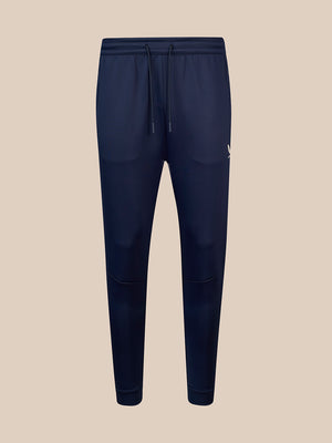 A pair of navy blue jogger sweatpants with an elastic waistband, matching drawstring, and a small white embroidered logo on the left hip, shown against a solid beige background.