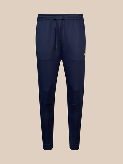 A pair of navy blue jogger sweatpants with an elastic waistband, matching drawstring, and a small white embroidered logo on the left hip, shown against a solid beige background.