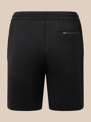 Black athletic shorts with an elastic waistband and a zippered side pocket, shown from the back on a solid beige background.