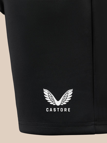 Close-up of a black garment leg featuring a white embroidered wing logo and the brand name 'CASTORE' near the hem, set against a light beige background.