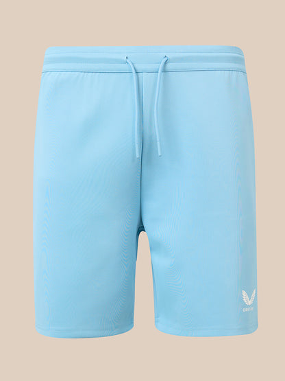 Light blue athletic shorts with a drawstring waist and a small white wing logo on the lower left leg, shown against a solid beige background.