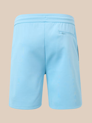 Light blue athletic shorts shown from the back, featuring an elastic waistband and a side pocket, set against a solid beige background.