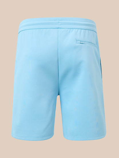 Light blue athletic shorts shown from the back, featuring an elastic waistband and a side pocket, set against a solid beige background.