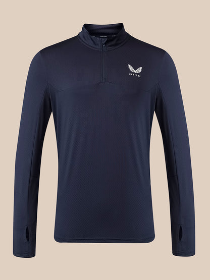 A navy blue long-sleeve quarter-zip athletic pullover with a white wing logo and the word 'Castore' on the left chest, displayed against a solid beige background.