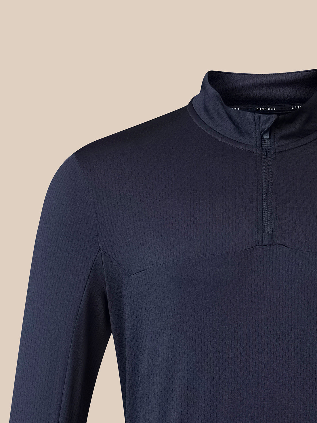 Close-up of a dark navy ribbed long-sleeve quarter-zip performance top on a model, showing the collar and upper chest against a solid beige background.