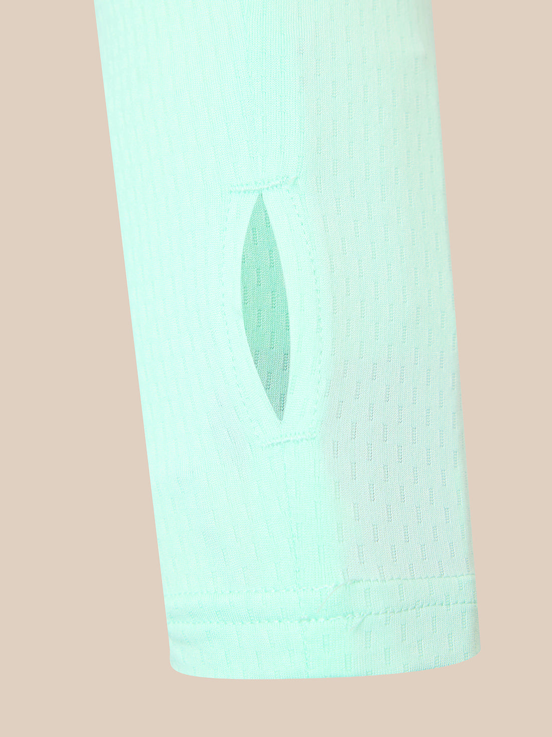 A close-up of a light mint green athletic sleeve with a vertical eyelet cutout, set against a solid pale peach background.