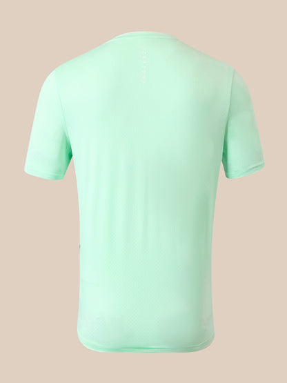 A mint green short-sleeve athletic t-shirt shown from the back, featuring a subtle vertical brand name on the upper back, set against a solid pale peach background.