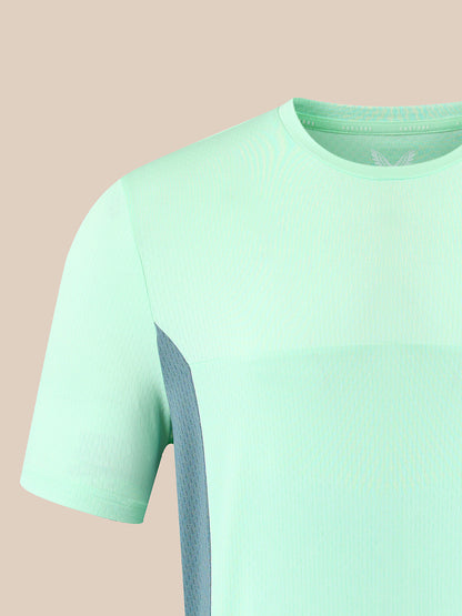 A close-up of a short-sleeve athletic t-shirt in mint green with a textured vertical panel on the side, shown against a solid pale peach background.