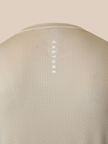 Close-up of the back of a light beige textured t-shirt with a vertical white 'CASTORE' logo printed on the center of the upper back, set against a solid beige background.