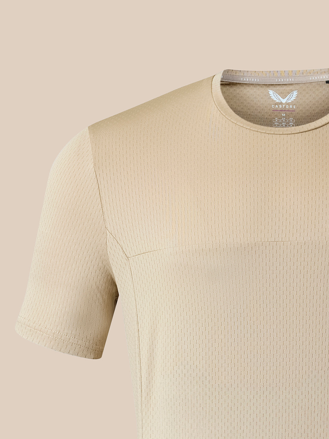 Close-up of a beige short-sleeve athletic top with a textured waffle knit fabric and a visible inner neck label reading CASTORE.