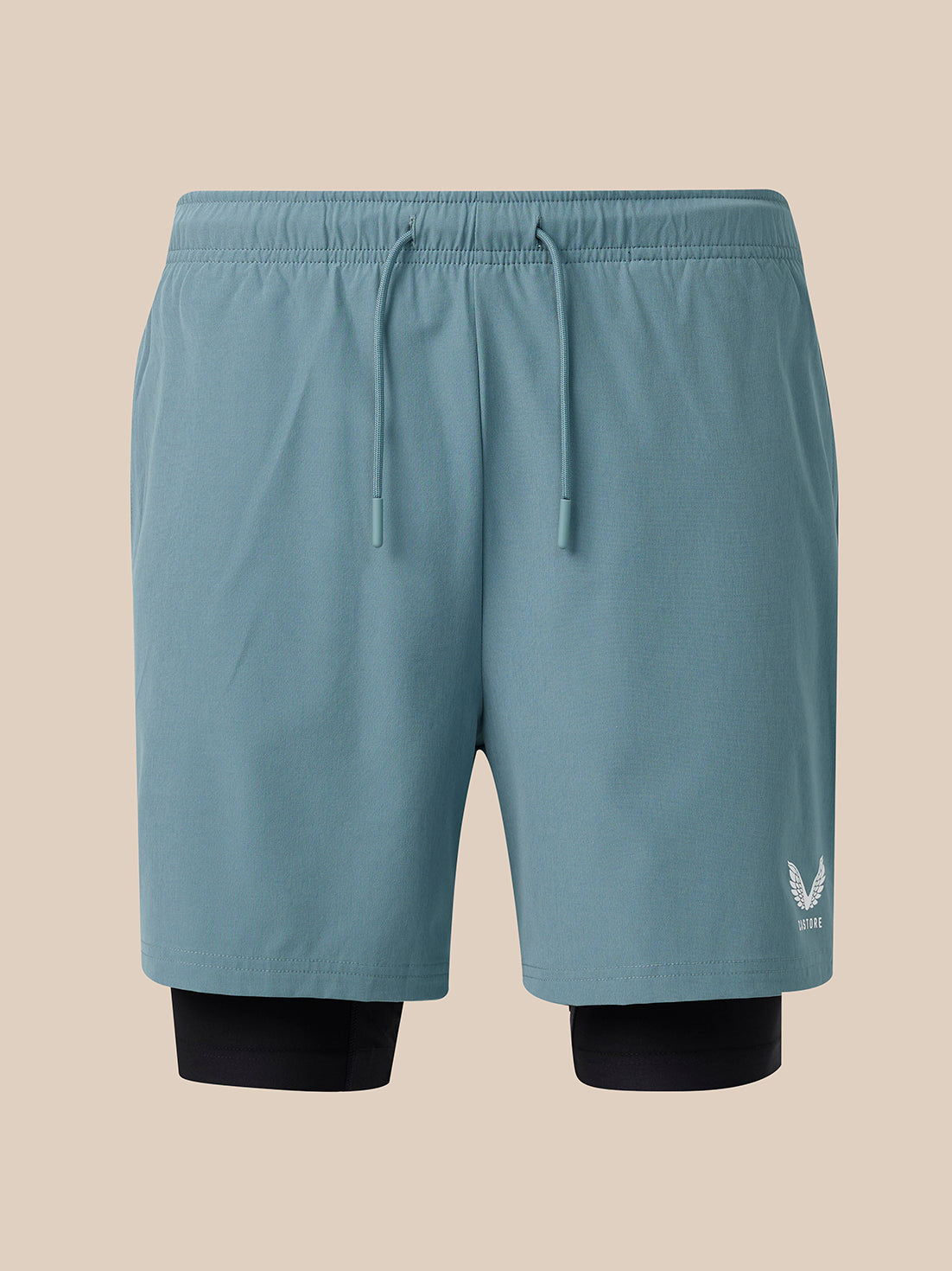 A pair of light blue athletic shorts with a matching elastic drawstring waist, featuring a black compression liner visible at the hem and a small white wing logo on the lower right leg, set against a solid beige background.