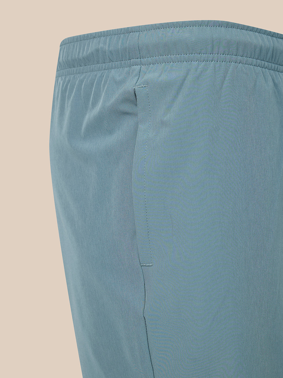 Close-up of a pair of light blue athletic shorts showing the elastic waistband and side seam against a solid beige background.