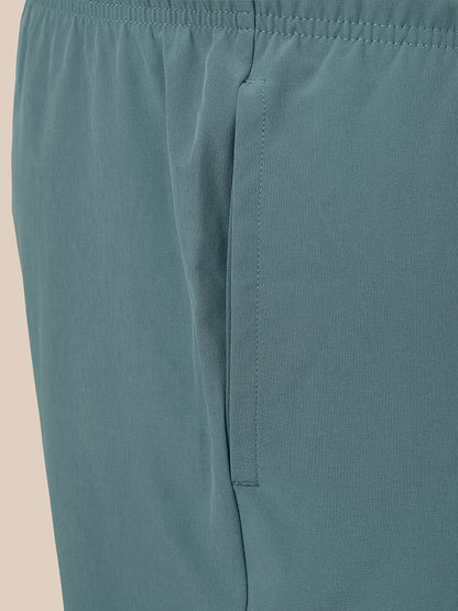 Close-up of a pair of muted teal athletic shorts showing the waistband, side seam, and a vertical welt pocket.