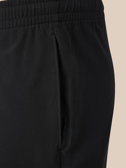 Close-up of black athletic pants showing the elastic waistband and side seam against a solid beige background.