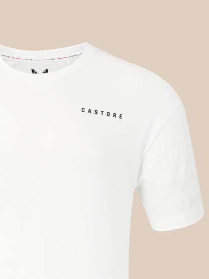 A close-up of a white short-sleeve crewneck t-shirt with the brand name 'CASTORE' printed in black capital letters on the left chest, set against a solid beige background.