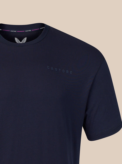 Close-up of a navy blue Castore short-sleeve t-shirt on a light beige background, showing the brand name and logo on the chest and inside the collar.
