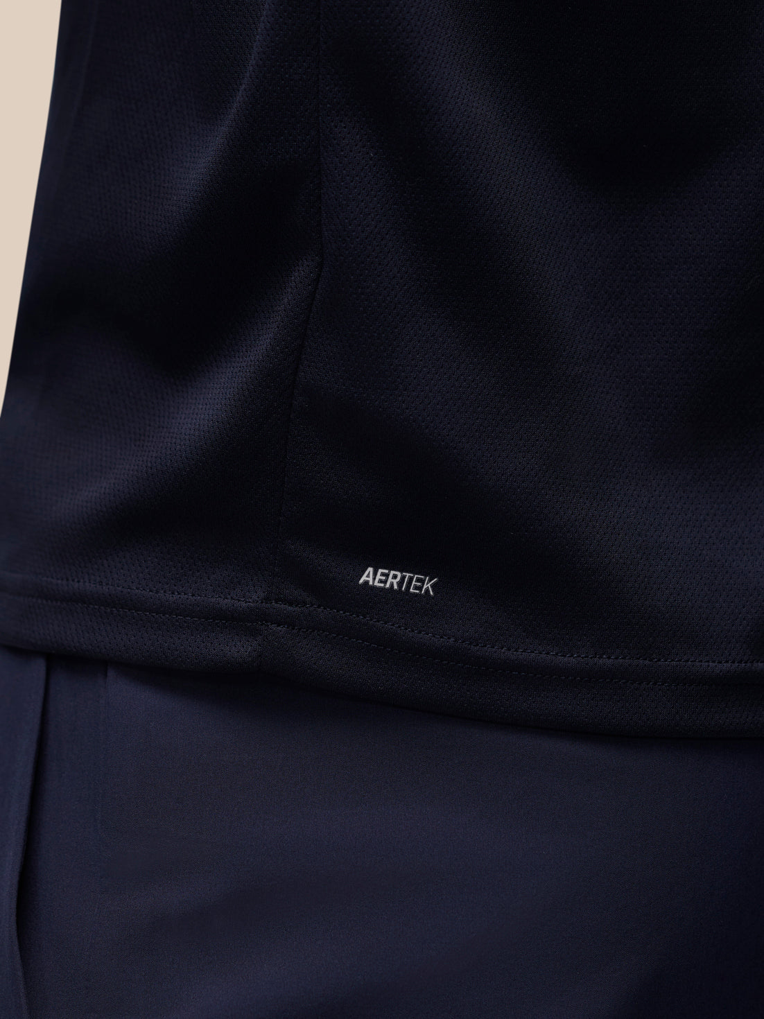 Close-up of a dark navy athletic top showing the AERTEK logo near the hem, with matching navy fabric below.