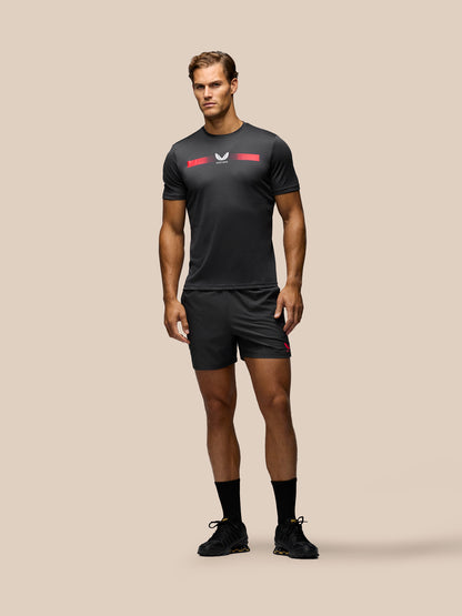 A man modeling a black athletic t-shirt and matching shorts set with red and white logo accents, standing against a solid beige background.