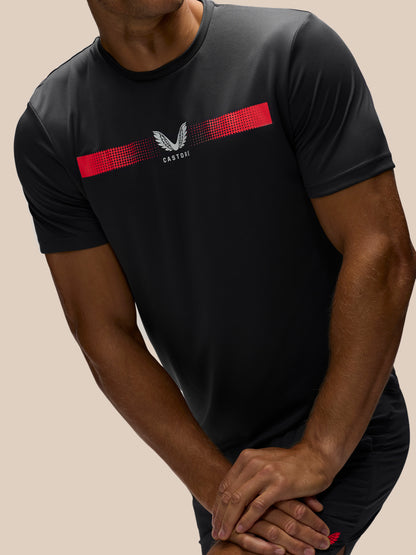 A man wearing a black short-sleeve athletic t-shirt with a red chest stripe and a white winged logo, shown from the neck down against a solid beige background.