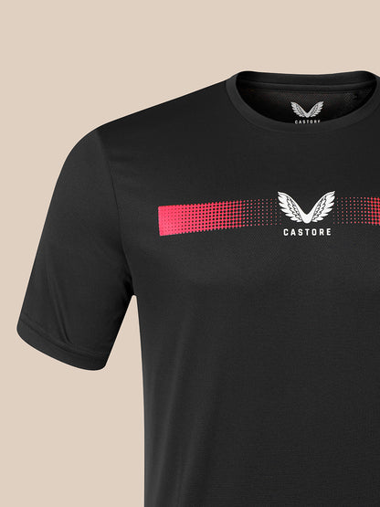 A close-up of a black Castore short-sleeve t-shirt featuring a white winged logo and a pink-to-white dotted horizontal stripe across the chest, set against a solid beige background.