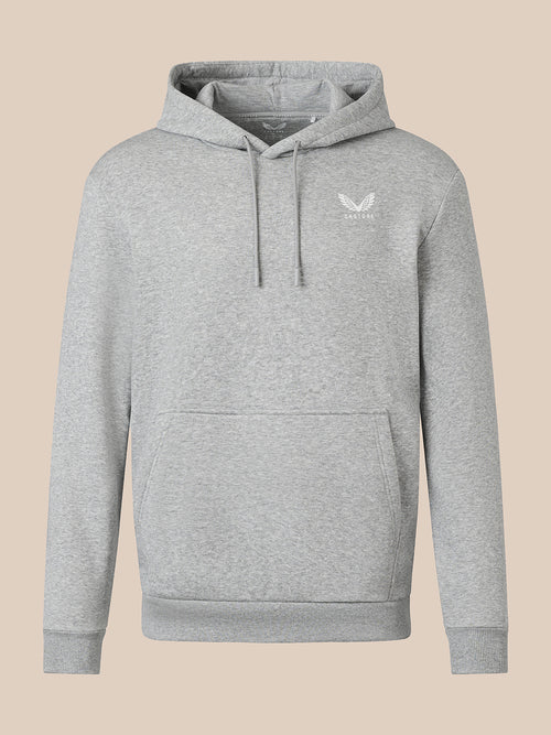 A light heather gray pullover hoodie with a small white embroidered winged logo on the left chest, displayed against a solid beige background.