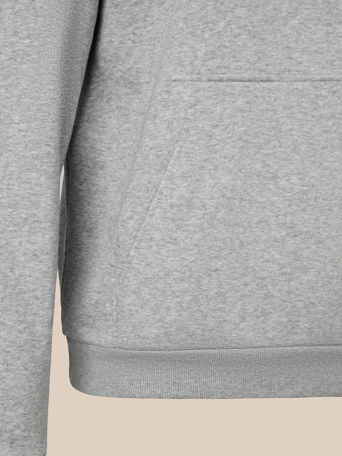 Close-up of a heather gray sweatshirt showing the chest pocket, sleeve, and ribbed hem against a light beige background.